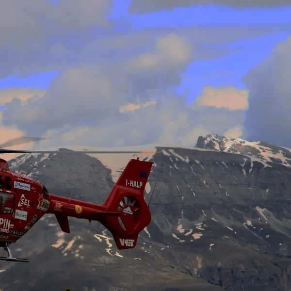 A red Aiut Alpin Dolomites rescue helicopter in flight in front of Dolomites peaks