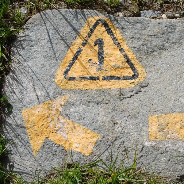 Yellow triangle trail marker painted on a grey rock along the Alta Via 1 hiking route