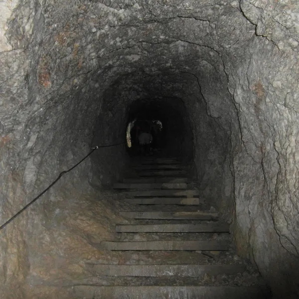 A wooden stair in the Anticima tunnel, cut into the rock, with a cable along the wall