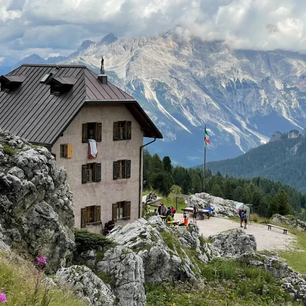Rifugio 5 Torri with the Cinque Torri rock formations and green forest under cloudy sky
