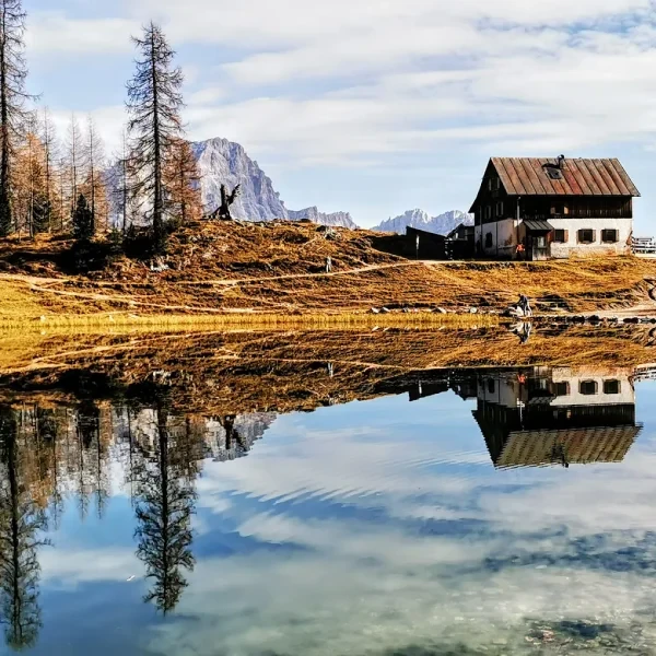 Rifugio Croda da Lago beside a mountain lake with hikers and autumn-colored trees
