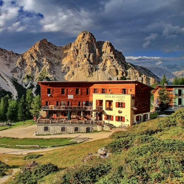 Rifugio Fanes with outdoor dining terrace and a cyclist arriving below rocky Dolomite peaks