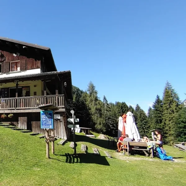 Rifugio Furio Bianchet on a grassy slope below forested peaks with an Italian flag flying
