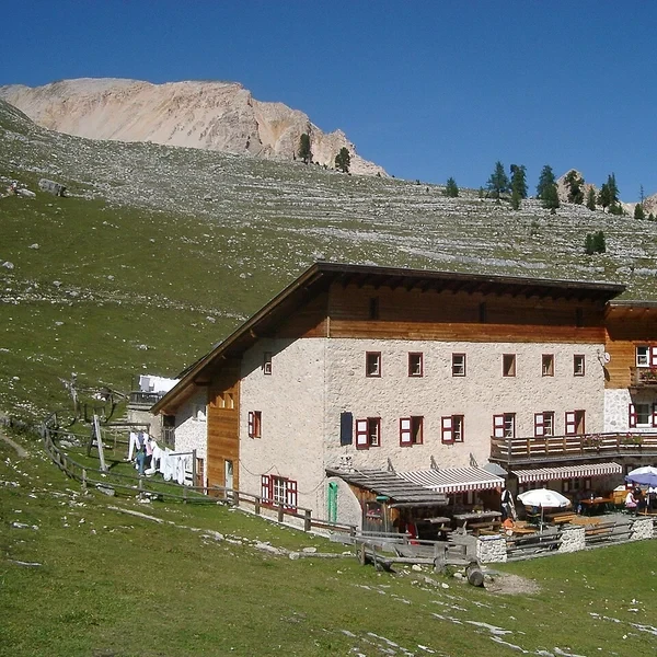 Rifugio Lavarella mountain hut with hikers approaching on a dirt path below grassy alpine slopes