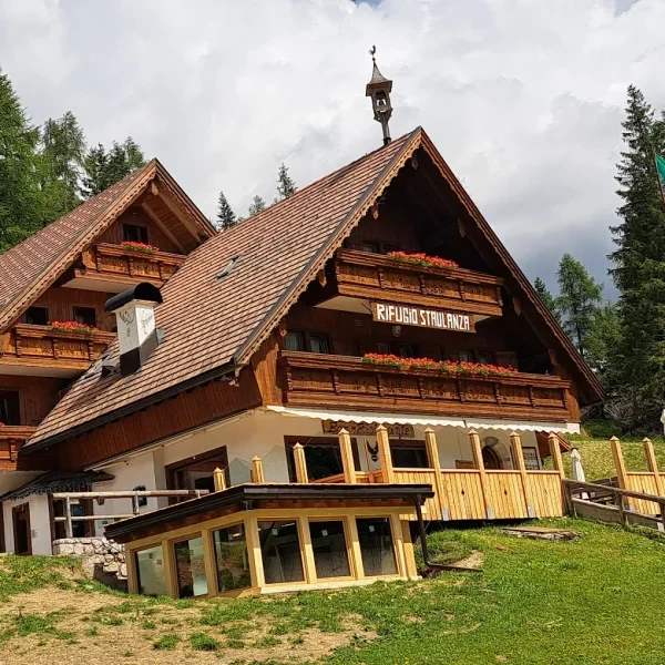 Rifugio Passo Staulanza wooden lodge set against a steep forested slope in summer