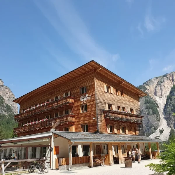 Berggasthaus Pederu nestled between steep rocky mountains with green slopes and pine trees