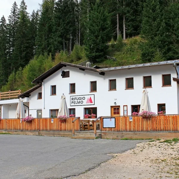 Rifugio Pelmo exterior with wooden picnic tables and snow on the ground below Monte Pelmo