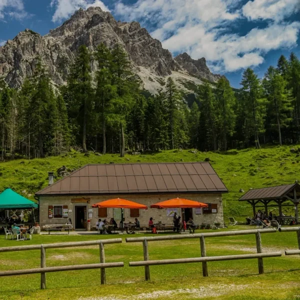 Malga Pramper hut with hikers on green pasture below rugged Dolomite peaks in Val Pramper