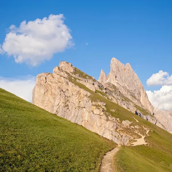 Hikers on a Dolomites trail with dramatic rocky peaks and green alpine meadows