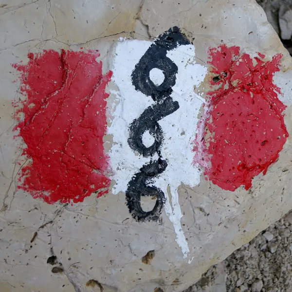 A red-white-red mark painted on a rock, with a black trail number on the white band